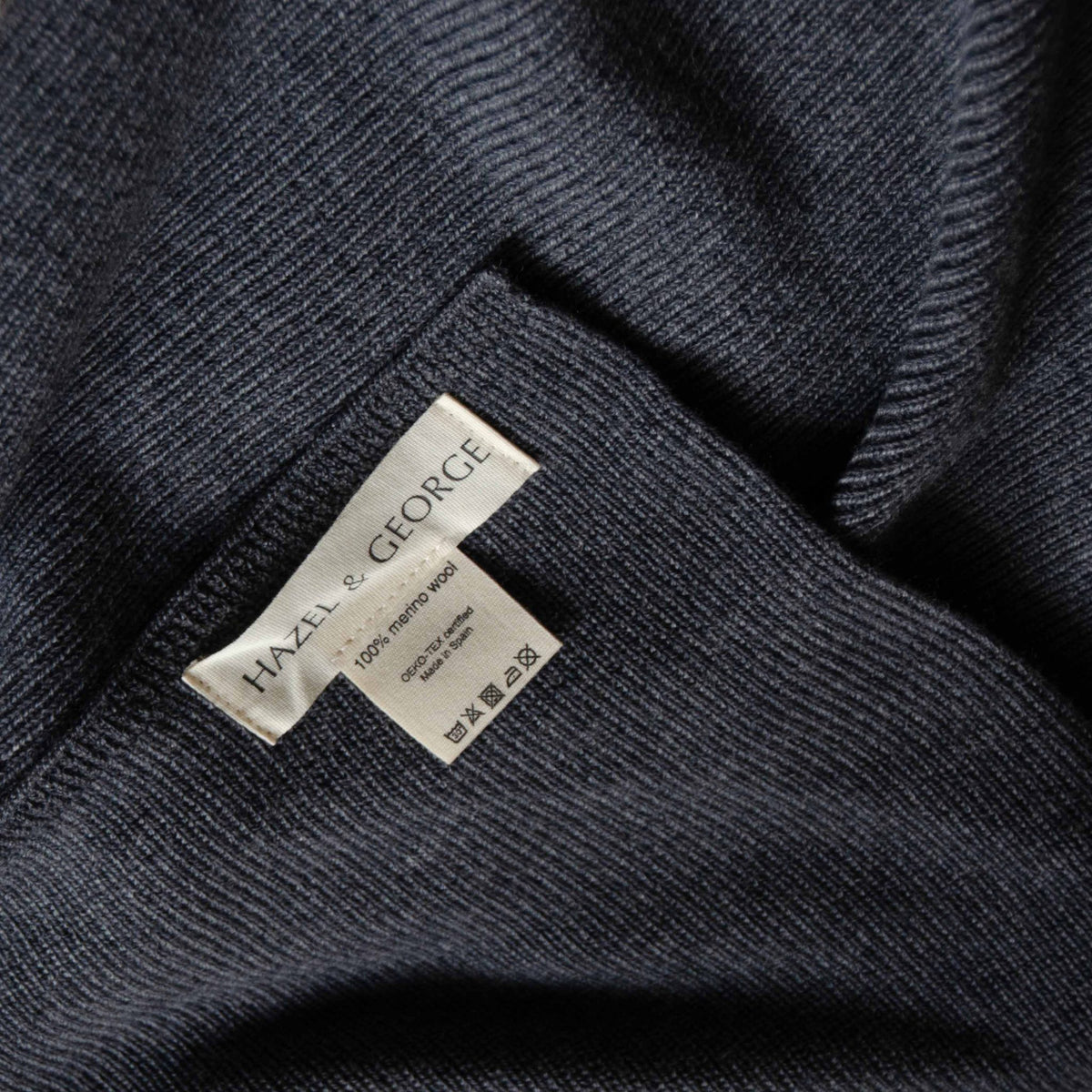 Close-up of the Hazel & George label reading 100% merino wool, Made in Spain, on the Hazel Merino Baby Blanket in Charcoal