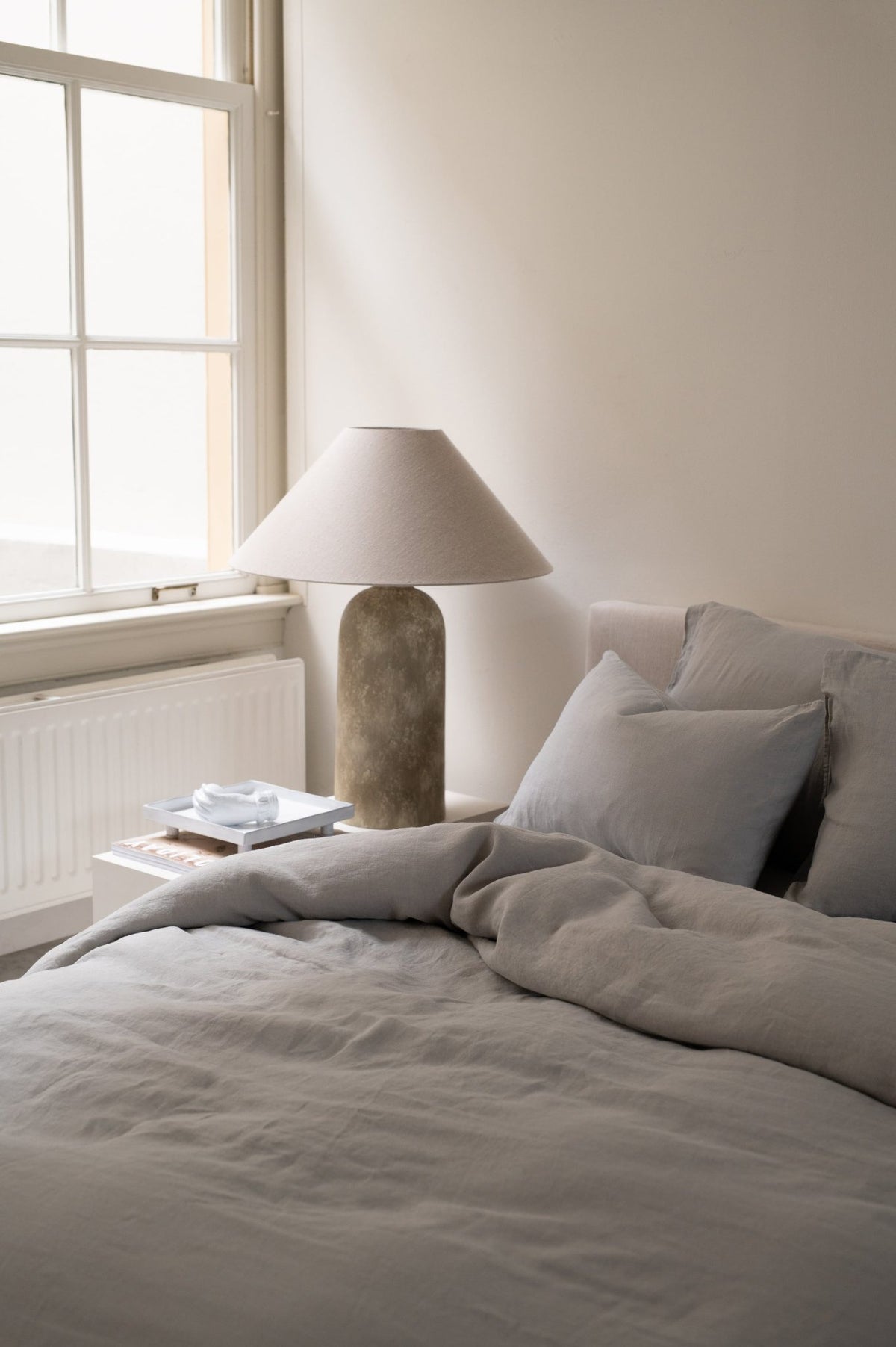Hazel & George Linen Duvet Cover in French Grey on a bed, with a nightstand and table lamp nearby