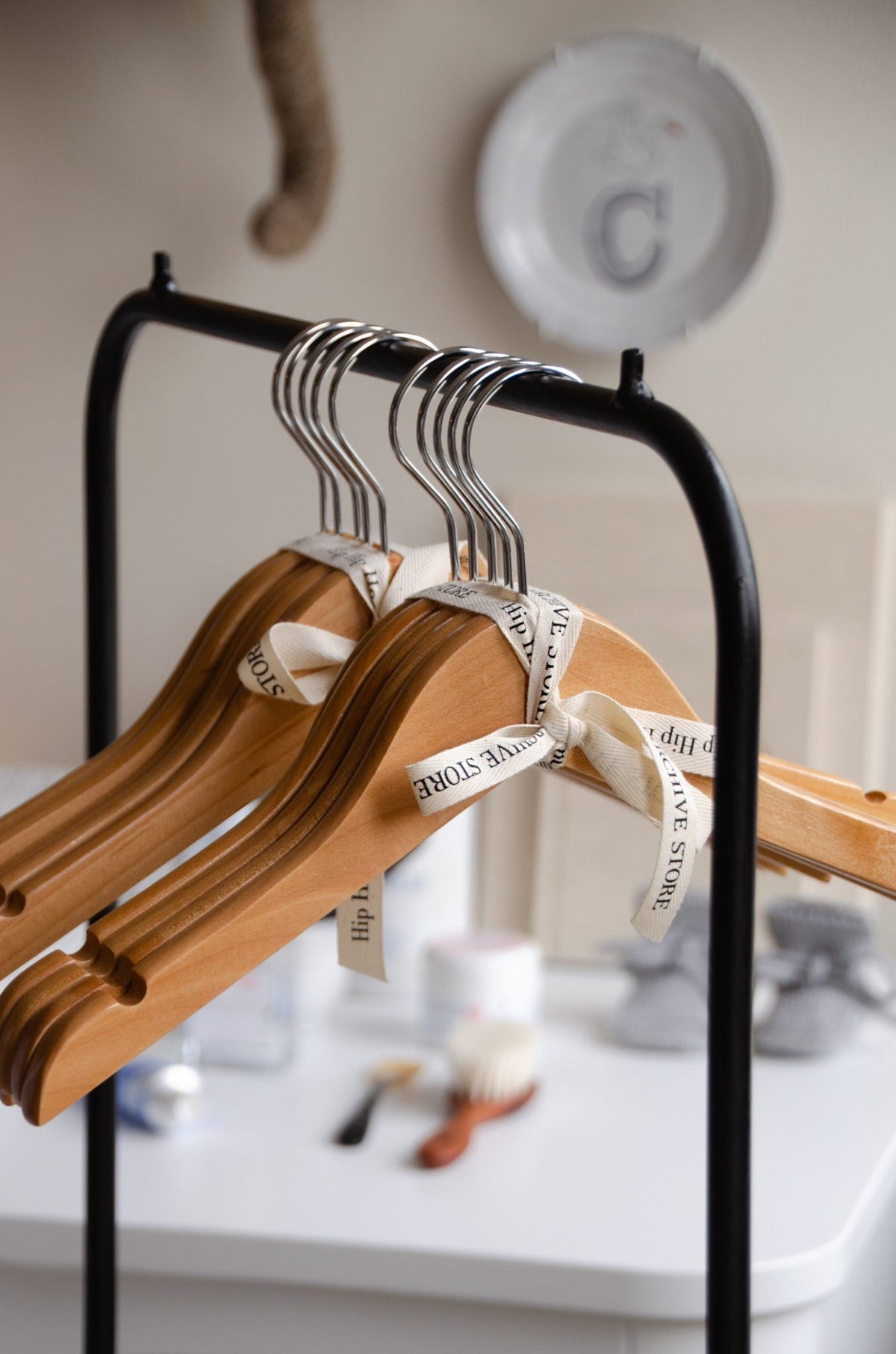 A bundle of Hazel & George Wooden Clothing Hangers tied with a The Archive Store ribbon, hanging on a clothing rack