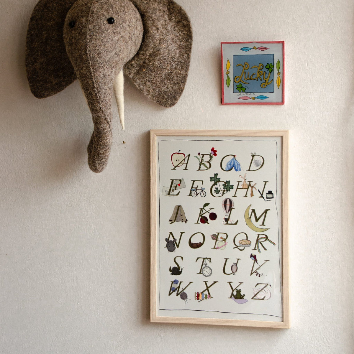 Ingelijste Hazel & George alfabetposter (limited A4-editie) aan de wand, naast een knuffelolifantenkop en een klein gekleurd naambordje