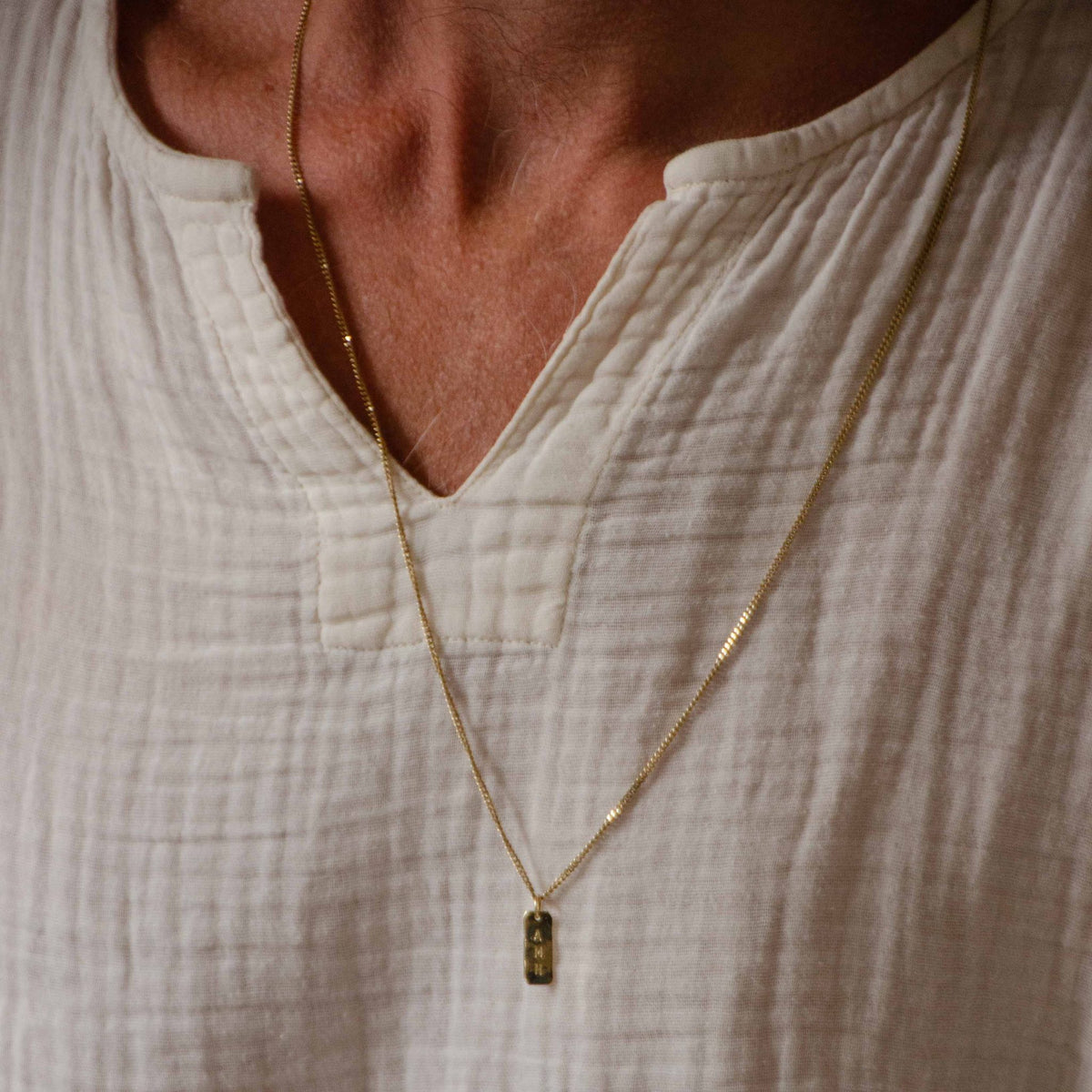 Hazel & George Necklace 14K Gold - 60 cm, man wearing a long gold necklace with a rectangular pendant engraved with the letters AMH