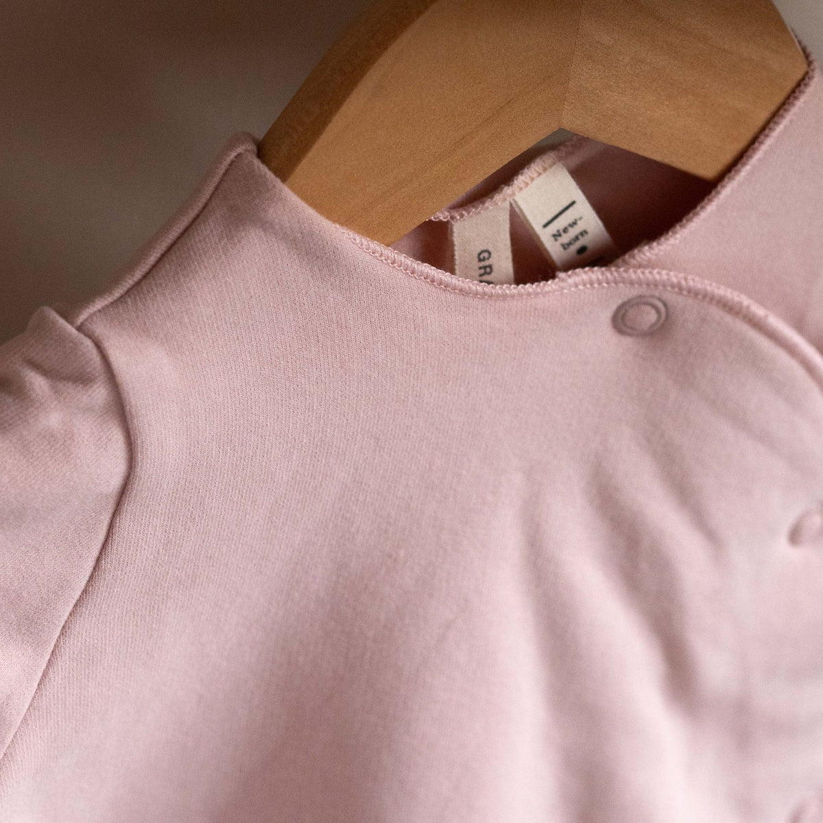 Close-up of the neckline and label of the Gray Label Newborn Suit in Faded Pink on a hanger