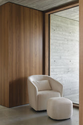 White armchair and ottoman against a wooden wall with a large window in the background