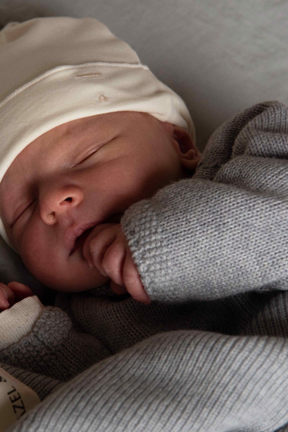 Gray Label Baby Beanie in Cream, worn by a sleeping newborn with a grey cardigan