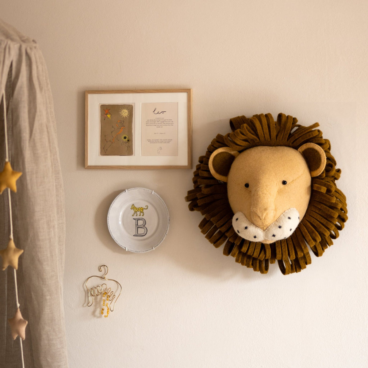 Ingelijste dubbele Hazel & George Leeuw-poster aan de wand in een kinderkamer, naast een knuffelleeuwenkop, een sierbordje met de letter B en een sterrenslinger