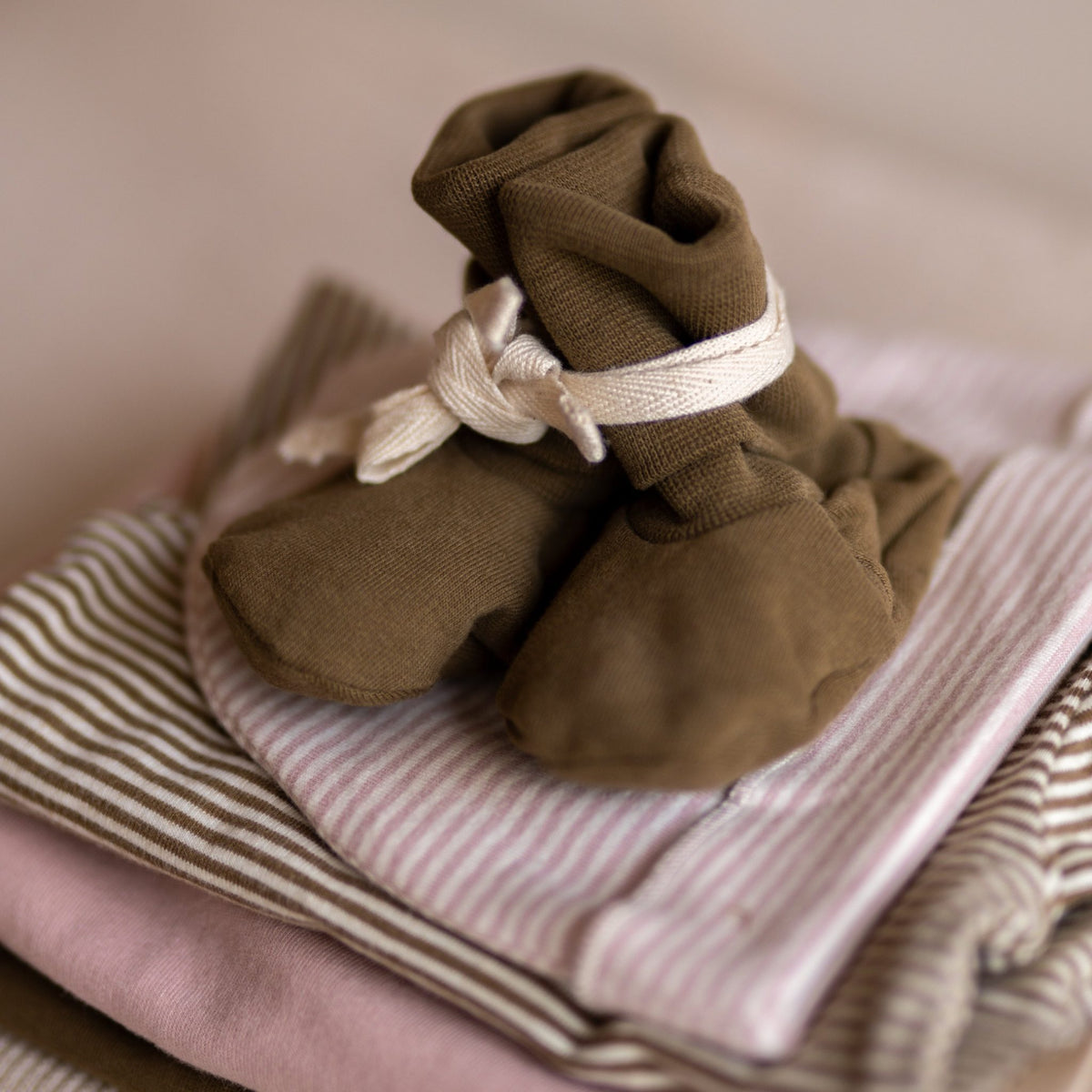 Close-up of the Gray Label Ribbed Baby Booties in Woody, styled on top of folded striped baby clothing
