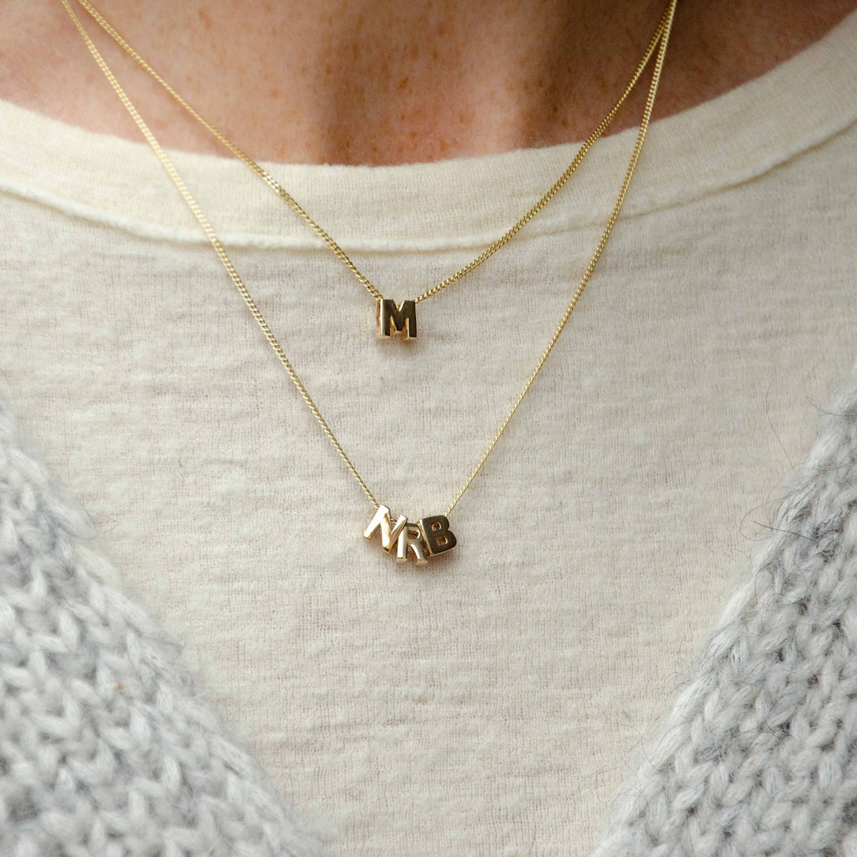 Hazel & George Chunky Initial 14K Gold, layered gold necklaces worn on a sweater with chunky letter charms spelling M and NRB