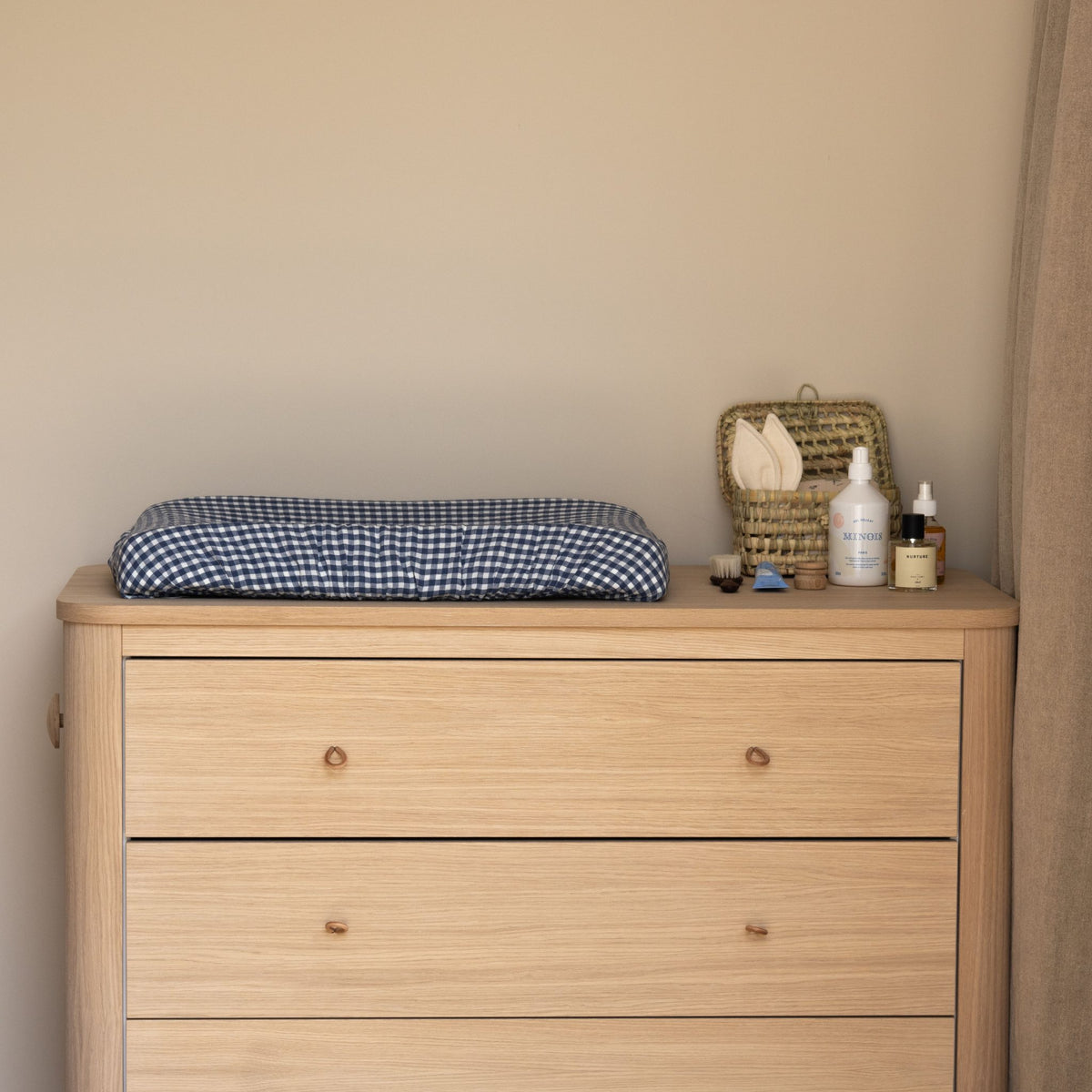Hazel & George Linen Changing Mat Cover in Vichy on a wooden dresser in a nursery, with a basket and baby care products nearby