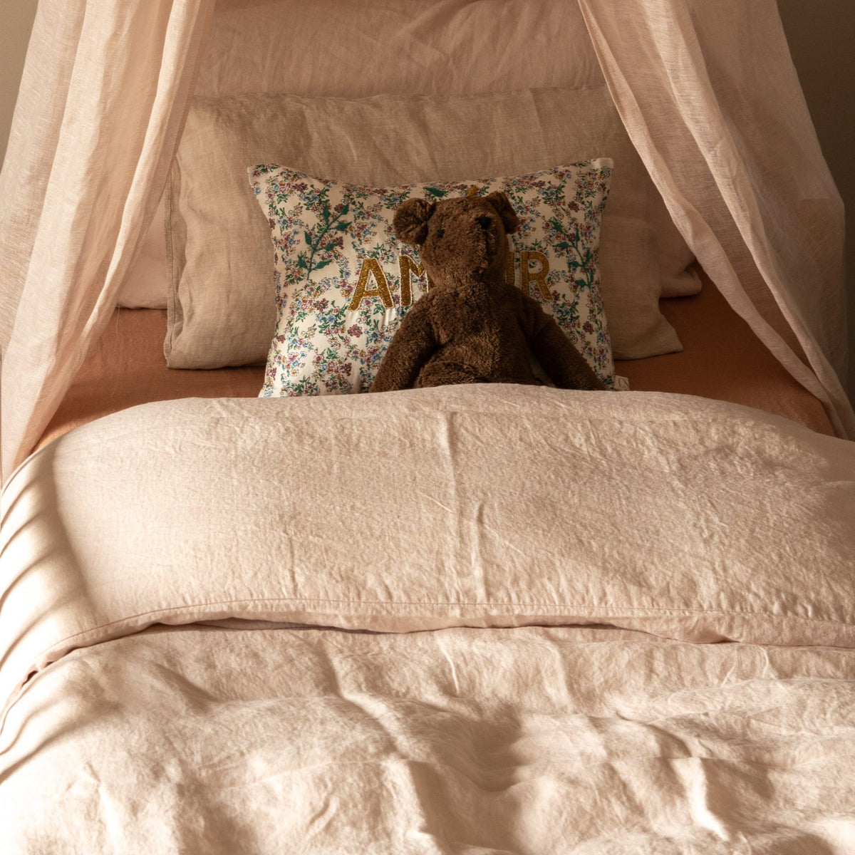 Hazel & George Linen Duvet Cover in Craie on a canopy bed, styled with a floral cushion and a teddy bear
