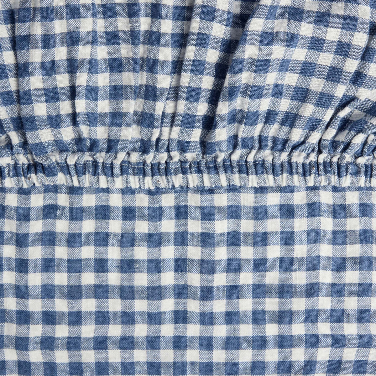Close-up of the elastic corner of the Hazel & George Fitted Sheet in Vichy, showing the woven blue-and-white check pattern