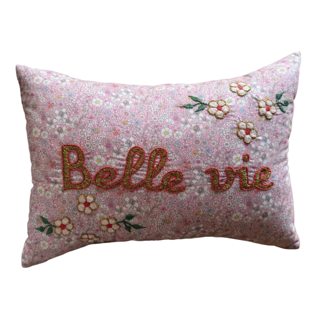 Decorative pillow with floral patterns and embroidered text on a beige surface.