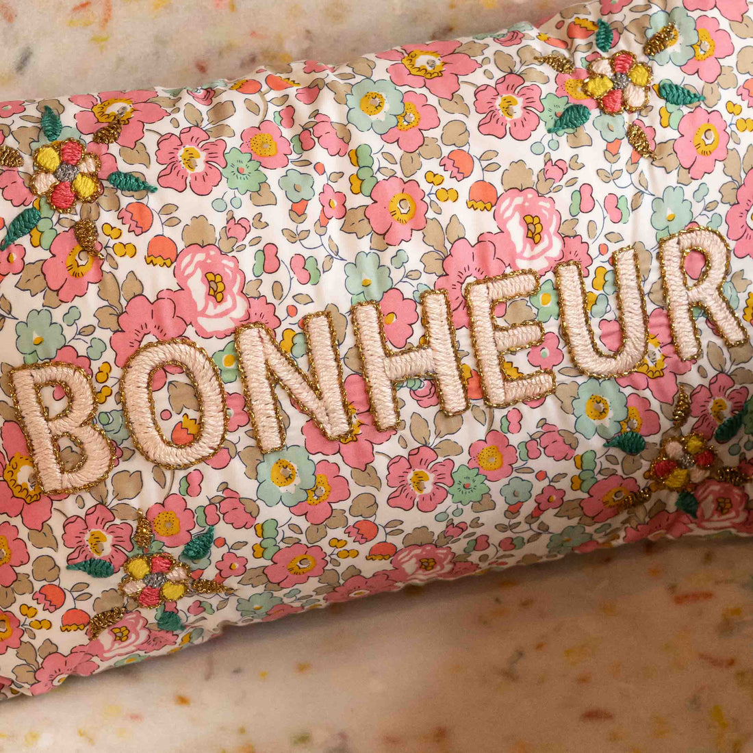 Floral-patterned pillow with embroidered letters spelling &