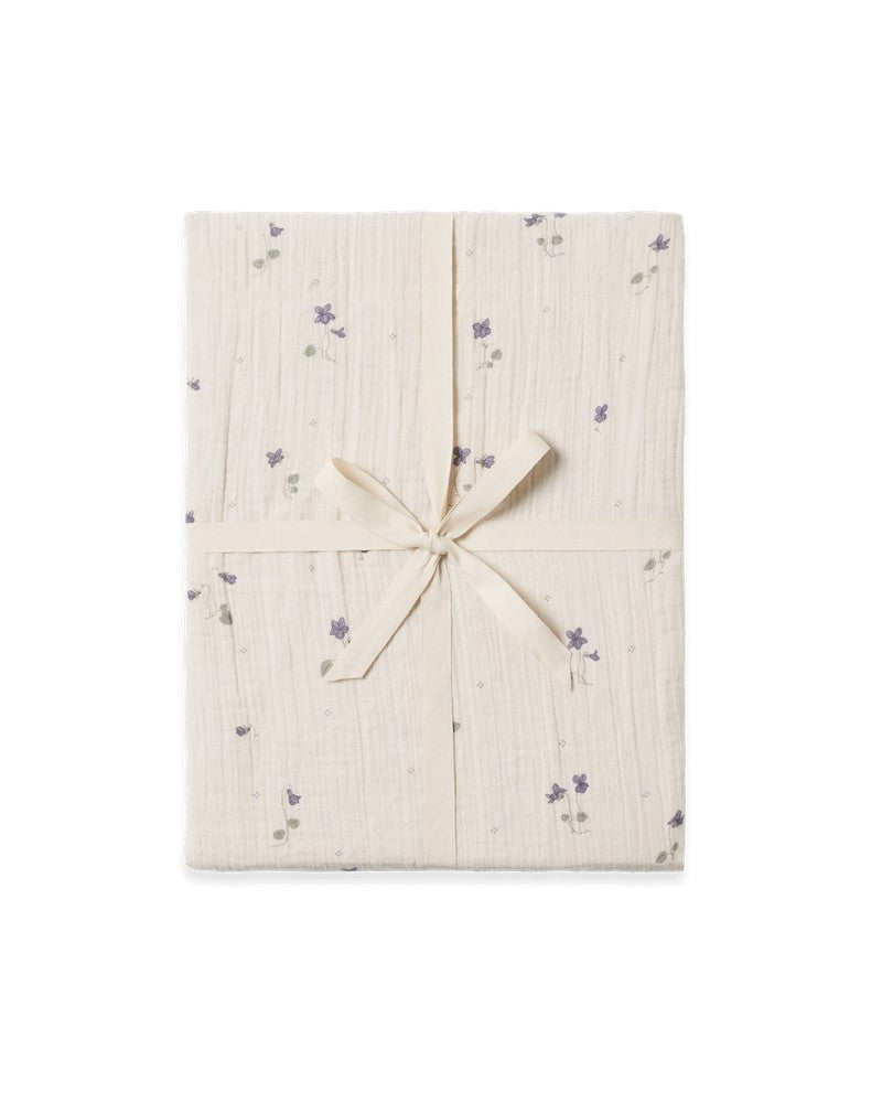 A folded Viola Muslin Fitted Sheet with a subtle floral pattern, tied with a ribbon.
