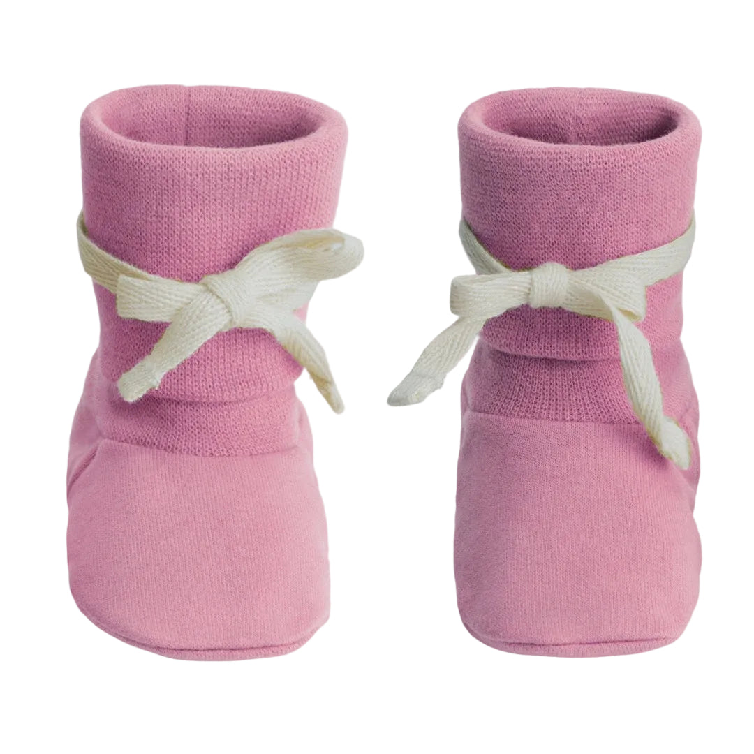 A pair of pink knit baby booties with white ribbon bows tied around the ankles