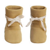 A pair of mustard yellow knit booties with white ribbon bows tied around the ankles