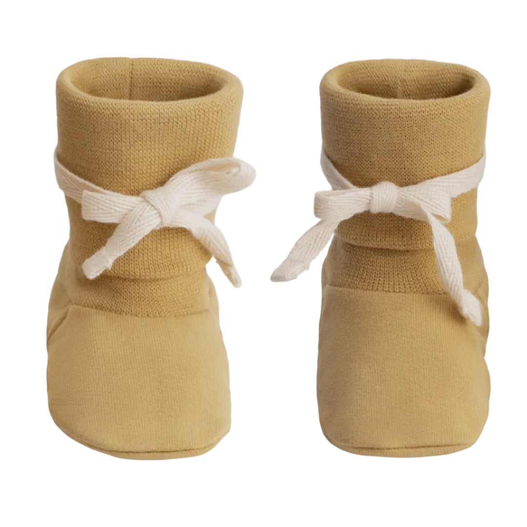 A pair of mustard yellow knit booties with white ribbon bows tied around the ankles