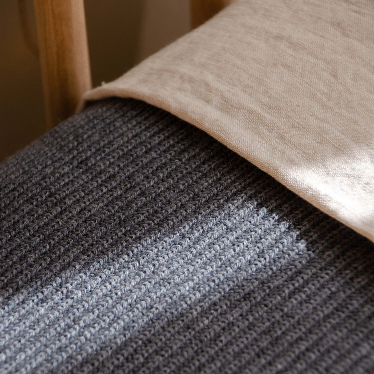Close-up of a Hazel &amp; George Georgia Merino Blanket in Charcoal draped over a wooden crib rail