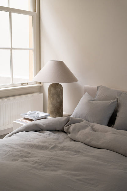 Hazel &amp; George Linen Duvet Cover in French Grey on a bed, with a nightstand and table lamp nearby