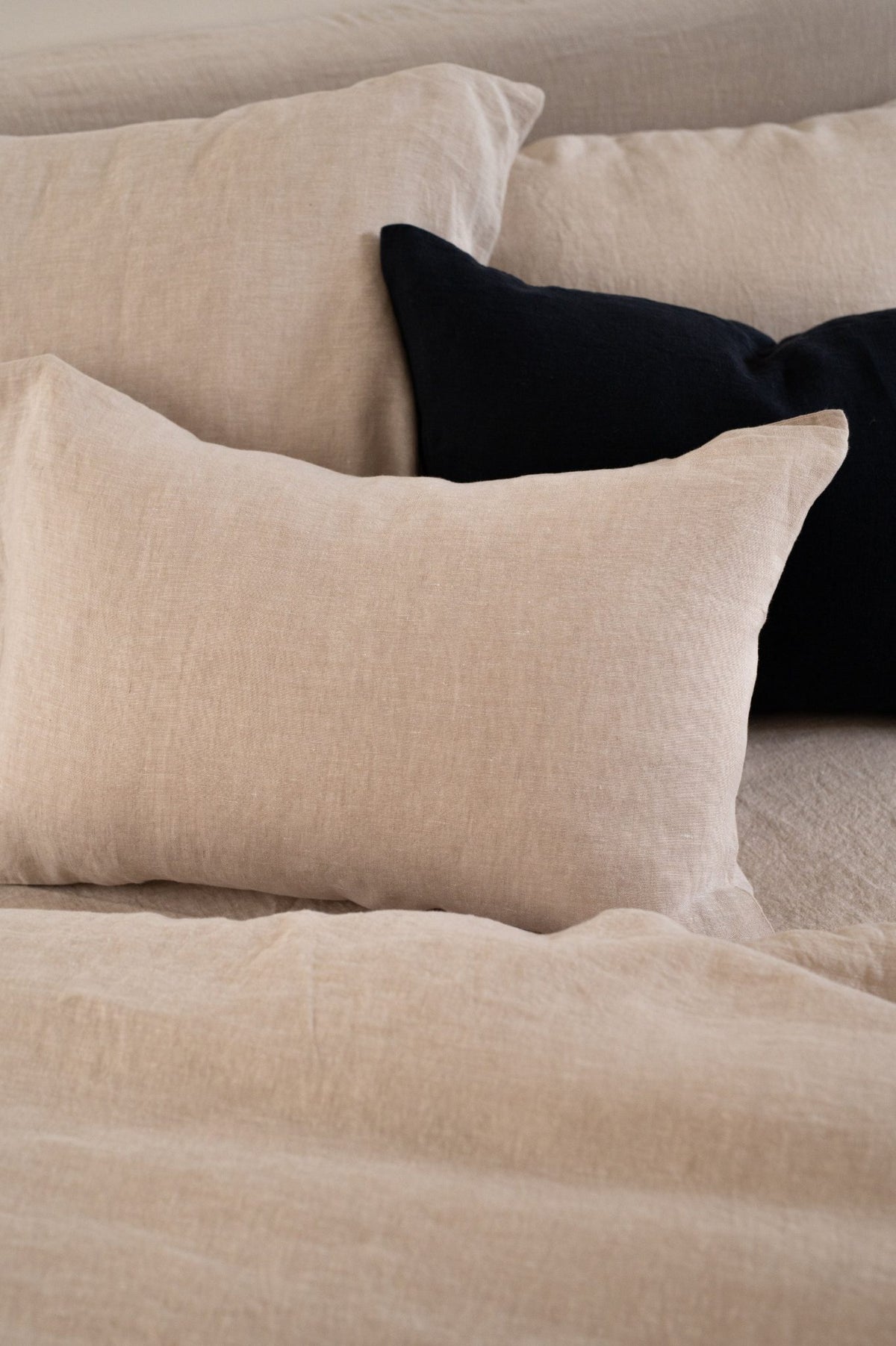 Bed styled with Hazel &amp; George linen bedding in Naturel, featuring a Naturel bolster pillow with a Naturel and an Off Black square pillow behind it