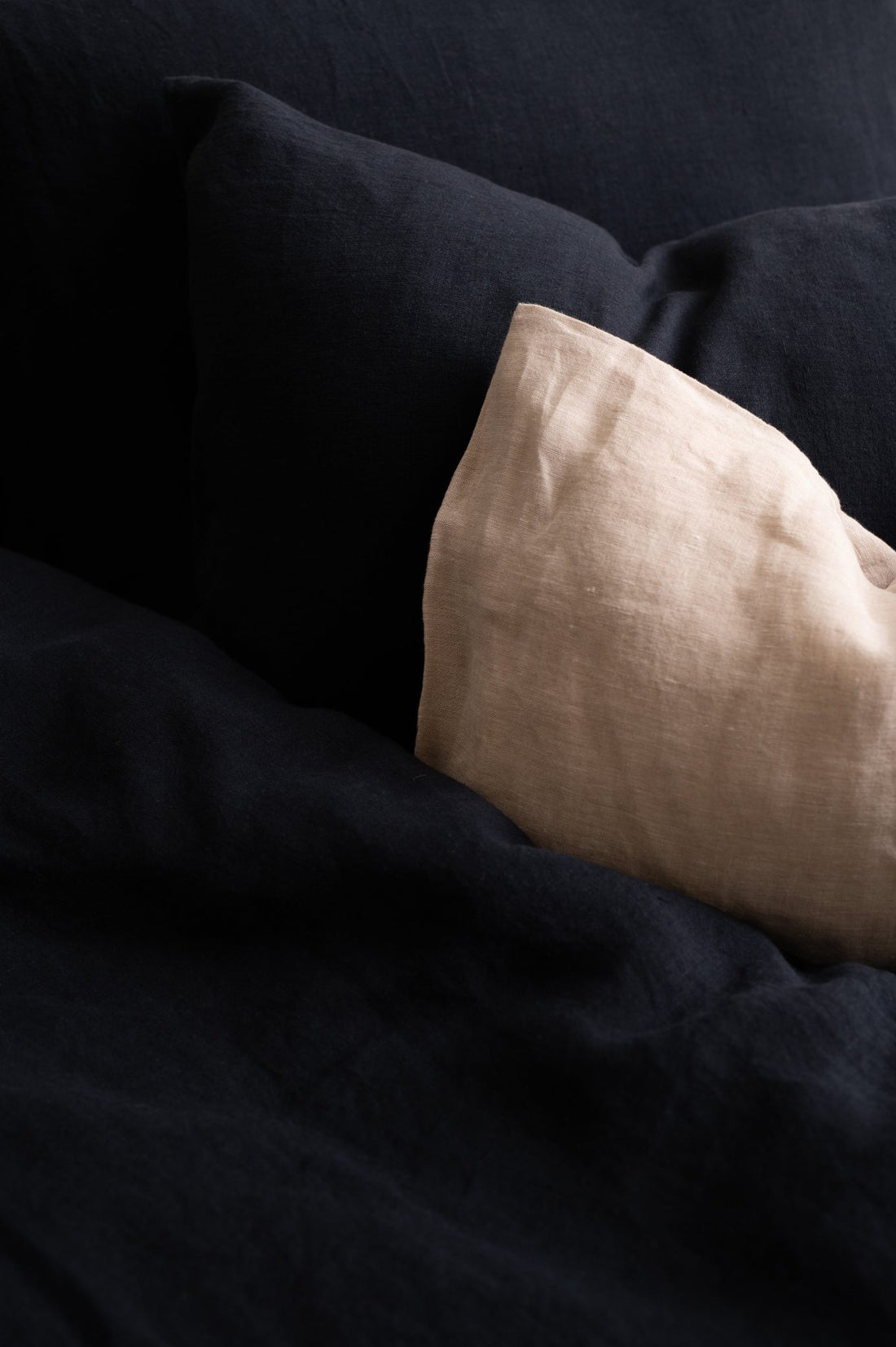Close-up of a Hazel &amp; George linen pillow in Off Black next to a Naturel pillow on a bed