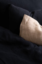 Close-up of a Hazel & George linen pillow in Off Black next to a Naturel pillow on a bed