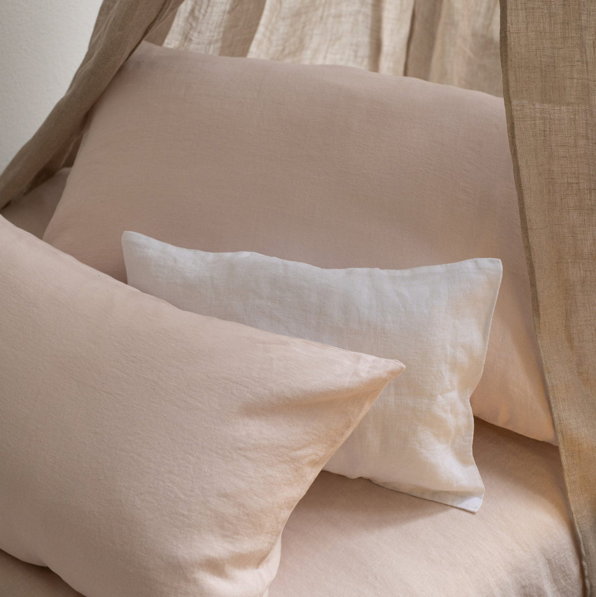 Bed styled with Hazel &amp; George linen pillows in Craie and a lighter pillow, under a canopy curtain