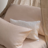 Bed styled with Hazel & George linen pillows in Craie and a lighter pillow, under a canopy curtain