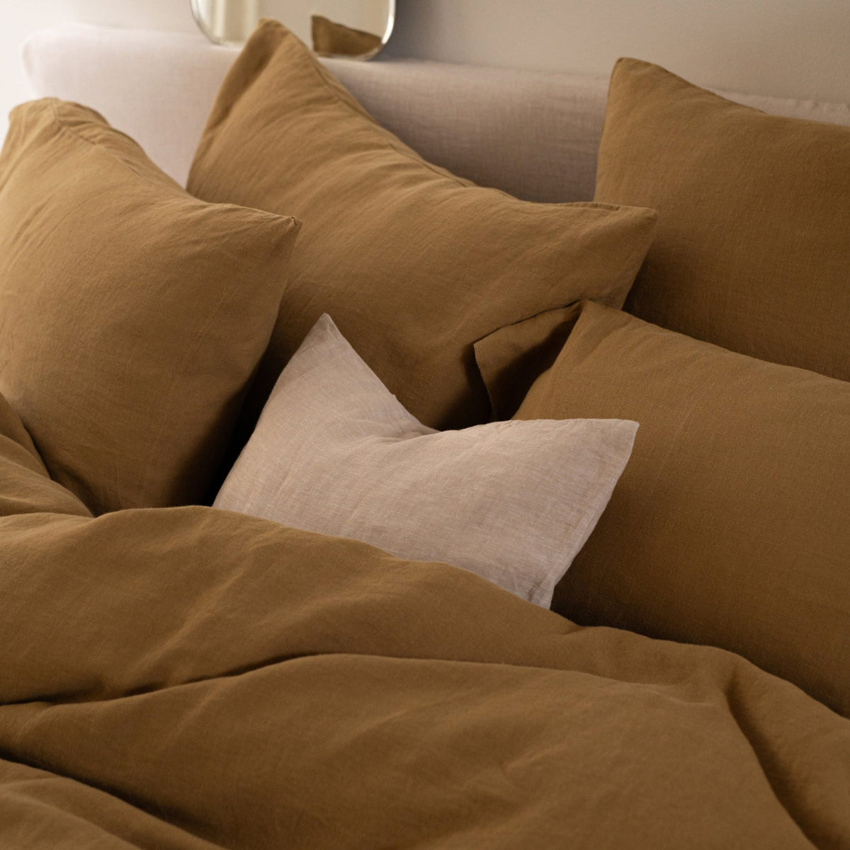 Bed styled with Hazel &amp; George linen bedding in Dore, several square Dore pillows with one Naturel pillow in front
