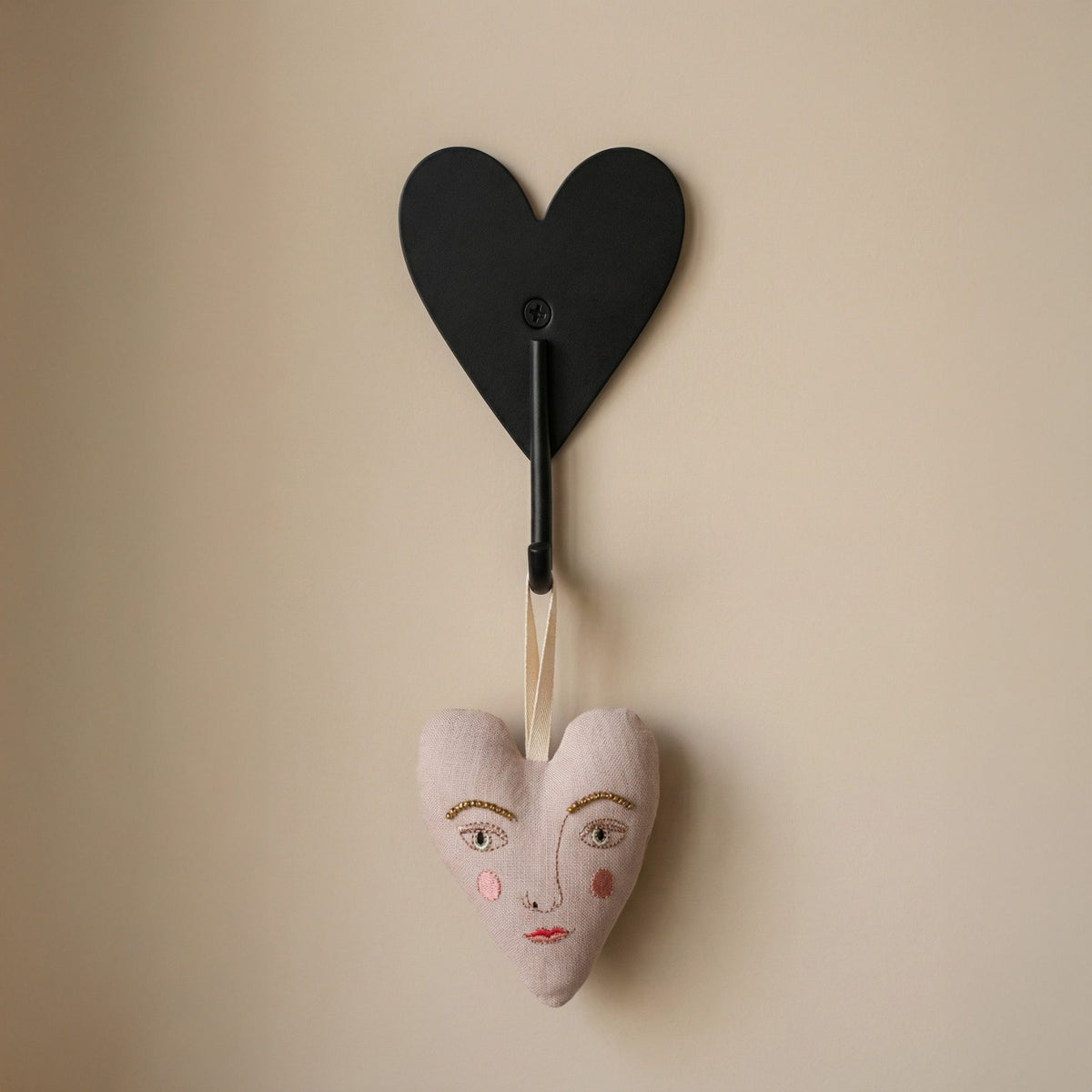 Hazel &amp; George Metal Heart Hook mounted on a wall, holding a decorative fabric heart ornament with an embroidered face