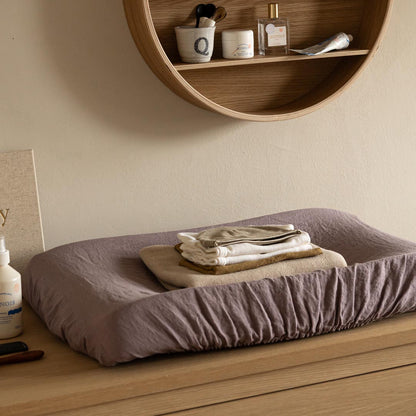 Changing table with folded towels on a wooden surface, shelf with items in the background