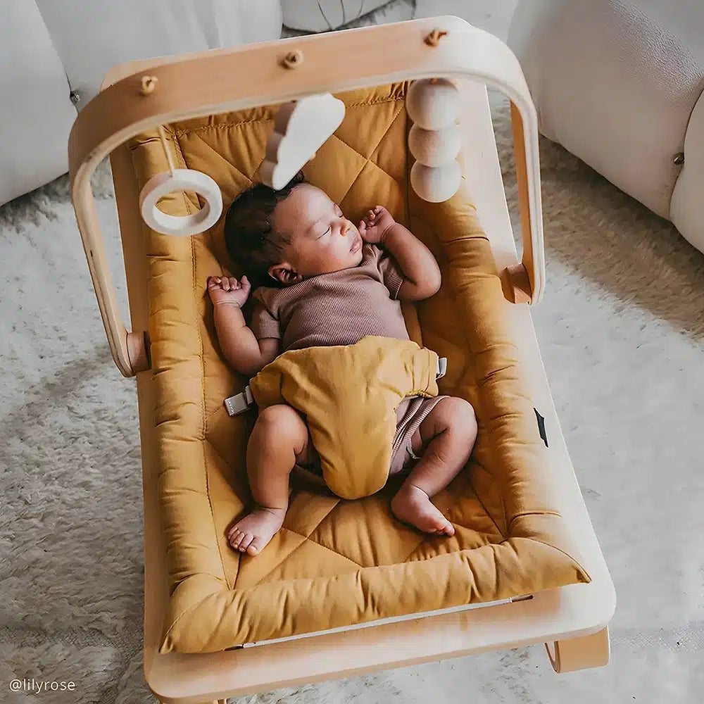 Baby lying in a Charlie Crane LEVO baby rocker, playing with the beech wood activity arch