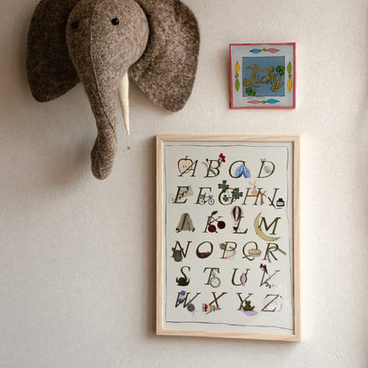 Ingelijste Hazel &amp; George alfabetposter (limited A4-editie) aan de wand, naast een knuffelolifantenkop en een klein gekleurd naambordje