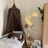 Hazel & George Linen Bed Canopy in Mosswood hanging above a white cot, with a moon-shaped light garland, a wardrobe and a teddy bear