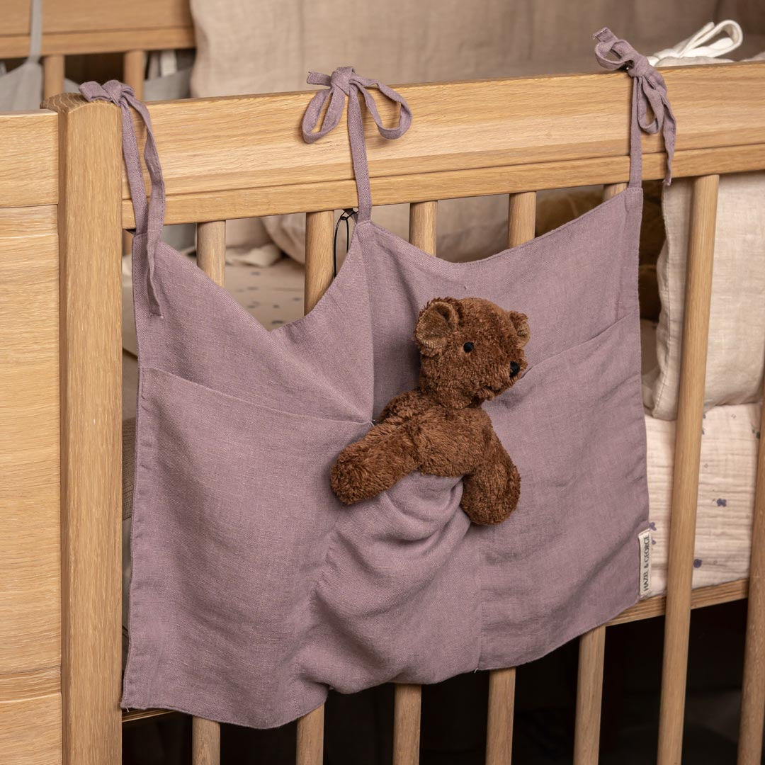 Purple hanging storage bag with a teddy bear inside attached to a wooden crib.