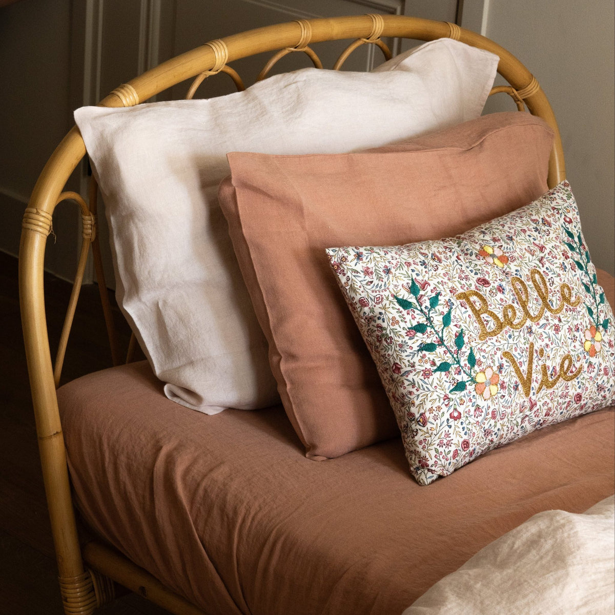 Rattan daybed styled with a white pillow, a Hazel &amp; George linen cushion in Cinnamon, and a decorative floral cushion