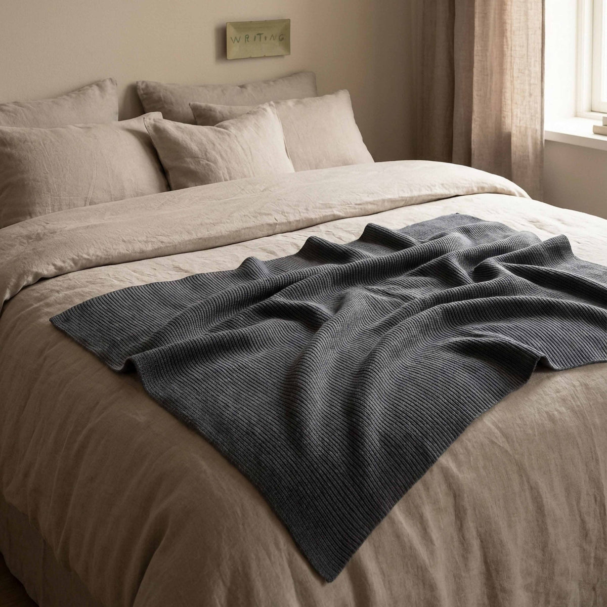 Hazel &amp; George Moss Large Merino Blanket in Charcoal draped over a bed with linen bedding