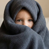 Toddler wrapped up in a Hazel & George Moss Large Merino Blanket in Charcoal, peeking out with only their eyes visible