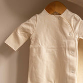 Close-up of the Gray Label Newborn Suit in Cream on a hanger, showing the snap button closure