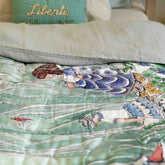 A reversible quilted blanket illustrated with a pond scenery, day on one side and night on the other.