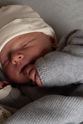 Gray Label Baby Beanie in Cream, worn by a sleeping newborn with a grey cardigan