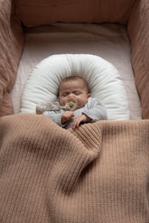 Sleeping baby in a crib with pink linen bedding, covered with a Hazel & George Abel Chunky Blanket in Biscuit