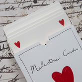 Close-up of the Milestone Cards box slightly open, showing the cards stacked inside, on a vintage script-print background