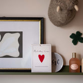 Milestone Cards box displayed on a shelf with framed art, a felt animal head, a ceramic clover and perfume bottles