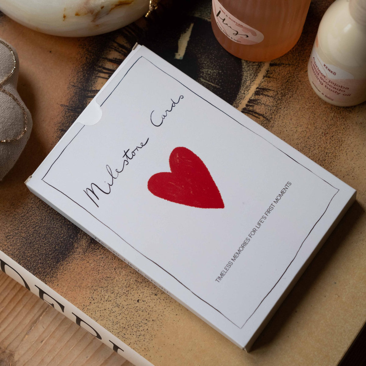 Milestone Cards box styled on a wooden crate with baby toiletries and a decorative woven ball in the background