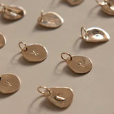 Close-up of loose Hazel & George Initial Hanger Large 14K Gold pendants engraved with different letters, laid out on a table