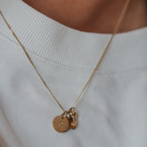 Hazel & George Initial Hanger Large 14K Gold, close-up of a gold necklace worn against a white top with a round pendant engraved with the letter G and a small heart charm