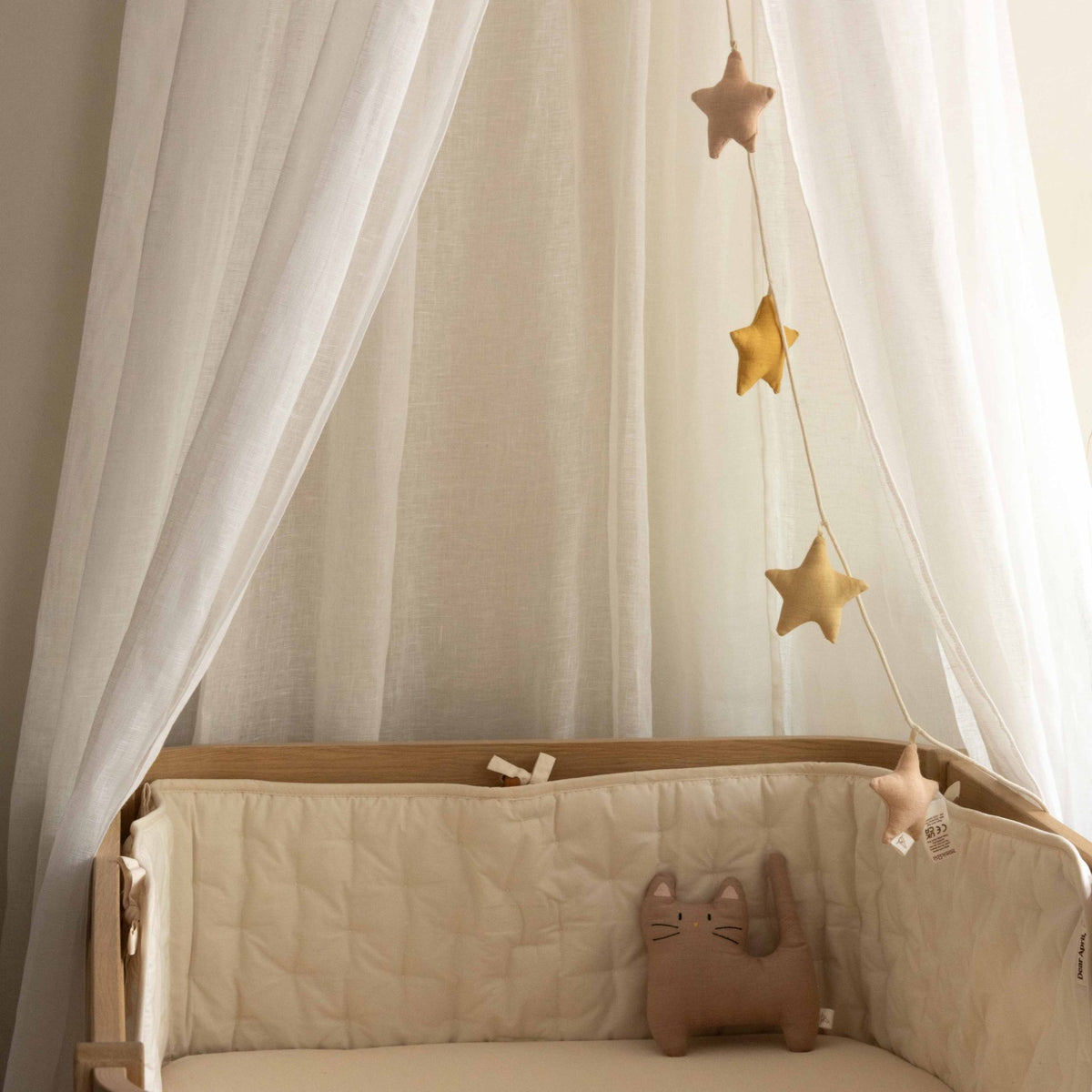 Nori Cot Bumper by Dear April in the Pure Nature print, styled in a crib with a star garland hanging above and a plush cat toy