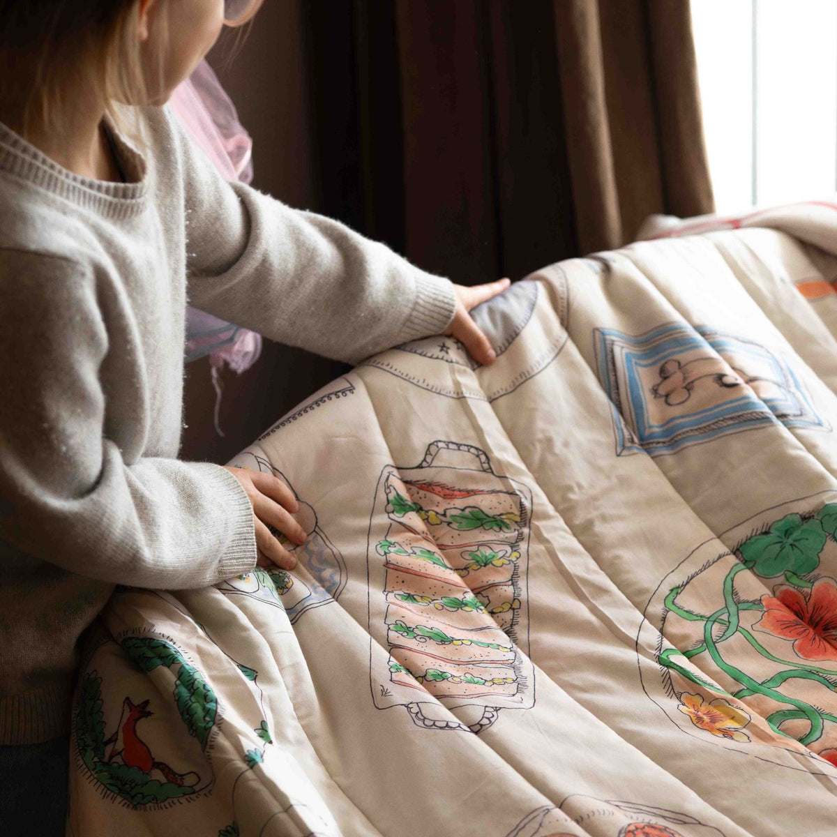 A reversible quilted blanket illustrated with woodland animals gathered around a festive table on one side and a plate motif on the other.