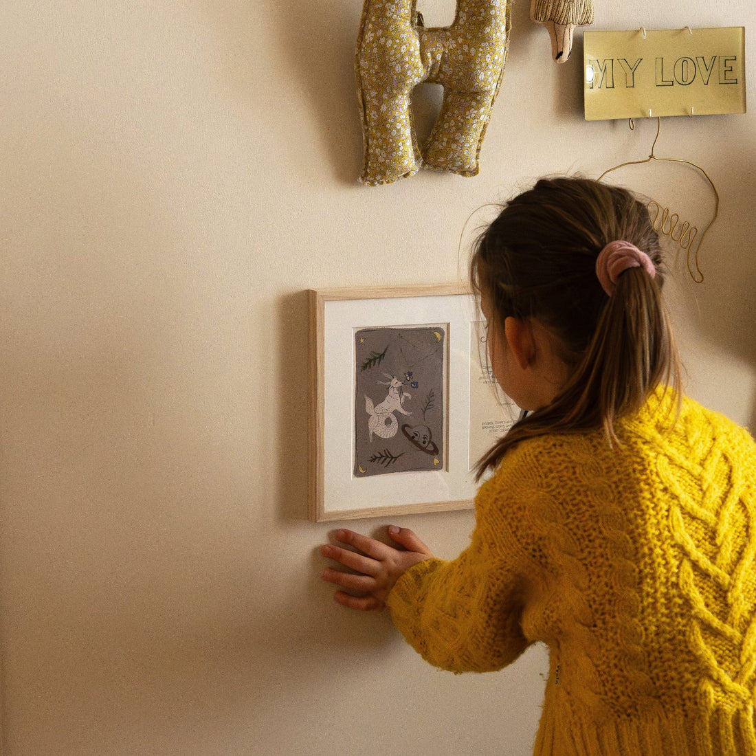 Ingelijste Hazel &amp; George Steenbok-poster aan de wand, met een kind dat de lijst aanraakt