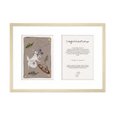 Ingelijste Hazel & George Steenbok-poster met twee panelen in één lichte houten lijst: links de illustratie met een steenbok, de planeet Saturnus en bloemen, rechts een tekstkaart met &